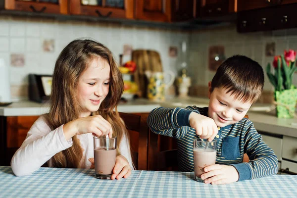 Children drink milk in the kitchen at the morning. Sister and brother prepare cocoa