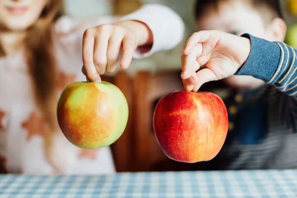 Children eat apples in the kitchen at the morning. The sister and brother hold the apples in their hands. Close-up