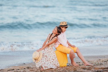 Çocuk oynamak ve eğlenmek sahilde. Deniz romantik hikaye. Bir kız ve bir erkek sırtlarını birbirlerine sarı bir bavul sahilde oturup