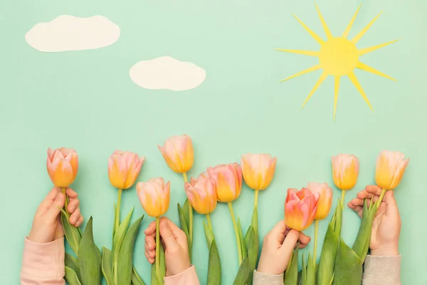 Beautiful flowers on the background of colored paper. Yellow tulips and green paper. Paper sun and clouds. Children\'s hands are holding a tulips
