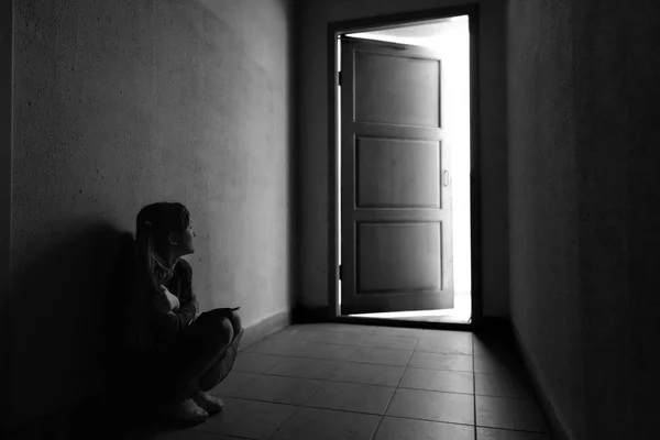光で開くドアの前に暗い廊下に座っている小さな女の子 恐怖と優柔不断 不確実性 先あなたを待って何ですか 一歩前進することに — ストック写真