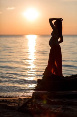 Gün batımında sahilde hamile bir genç kız silüeti