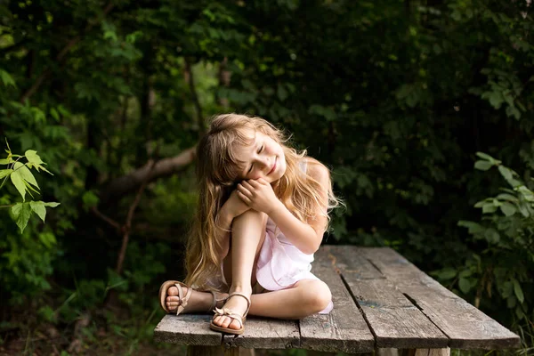 Pretty smiling pensive girl sitting on the old bridge in the forest