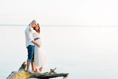 Denizde güneşli yaz akşamı aşık genç hamile Çift