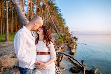 Genç hamile çift sahilde güneşli yaz akşamı aşık