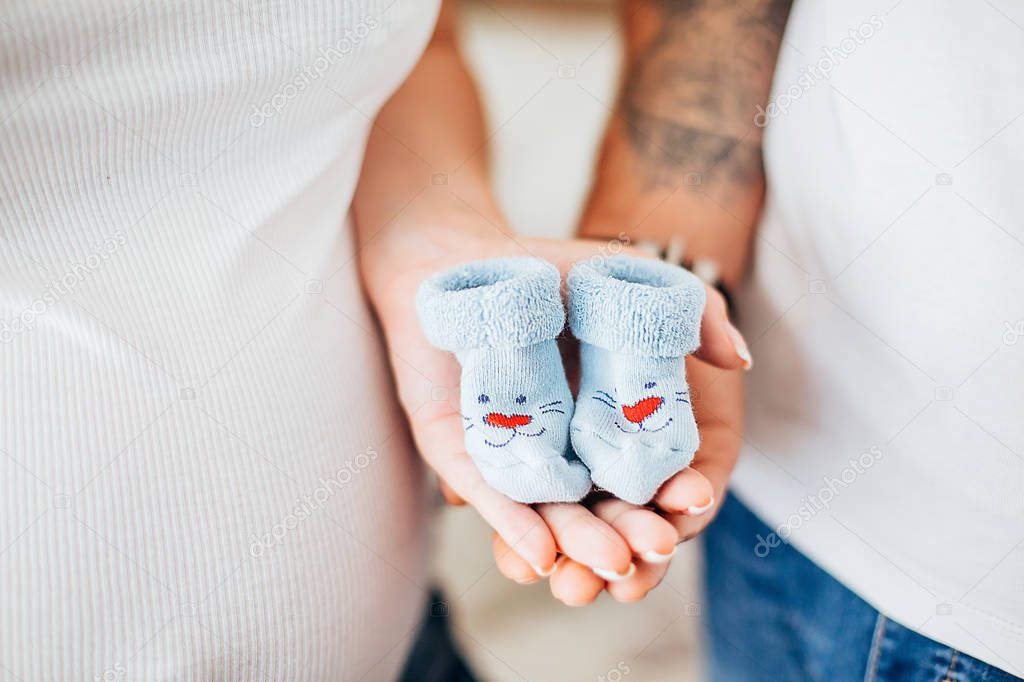 hands and torso of a pregnant woman and her husband, are holding new born baby socks 
