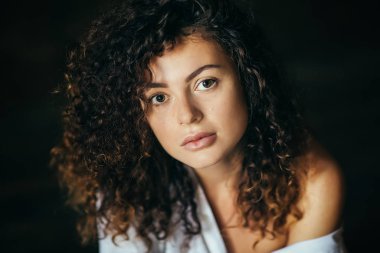 Karanlık bir stüdyoda güzel bir genç kız portresi. Kıvırcık saçlı. Açık gömlek ve iç çamaşırı