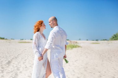 Düğün günü. Mutlu genç bir çift aşık kumlu kıyı yürüyüş. Kel damat ve Kızıl saçlı gelin.