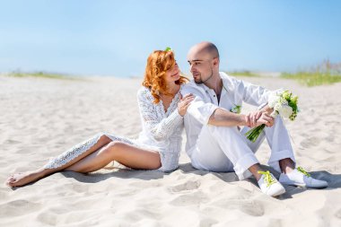 Düğün günü. Mutlu genç bir çift aşık kumlu kıyı yürüyüş. Kel damat ve Kızıl saçlı gelin.