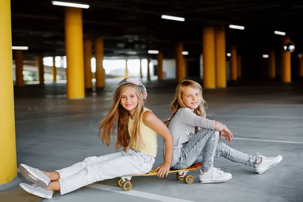 Two beautiful girls skateboarding, having fun and playing in the parking lot. Street photo shoot