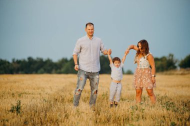 Mutlu aile kavramı. Anne ve babanın oğlu. Güneşin altında mutlu bir aile var. Anne, baba ve oğul gün batımında mutlu yürüyüşler, ebeveynler bebeği tutuyor.. 