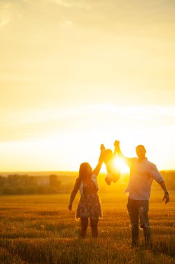 Mutlu aile kavramı. Anne ve babanın oğlu. Güneşin altında mutlu bir aile var. Anne, baba ve oğul gün batımında mutlu yürüyüşler, ebeveynler bebeği tutuyor.. 