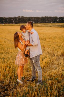 Mutlu aile kavramı. Anne ve babanın oğlu. Güneşin altında mutlu bir aile var. Anne, baba ve oğul gün batımında mutlu yürüyüşler, ebeveynler bebeği tutuyor.. 