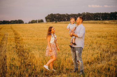 Mutlu aile kavramı. Anne ve babanın oğlu. Güneşin altında mutlu bir aile var. Anne, baba ve oğul gün batımında mutlu yürüyüşler, ebeveynler bebeği tutuyor.. 
