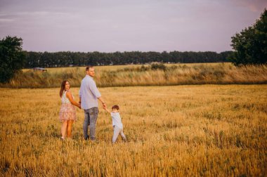 Mutlu aile kavramı. Anne ve babanın oğlu. Güneşin altında mutlu bir aile var. Anne, baba ve oğul gün batımında mutlu yürüyüşler, ebeveynler bebeği tutuyor.. 