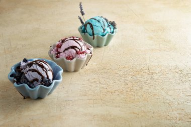 Bej arka planda renkli seramik kaselerde ahududu, lavanta ve hanımeli ile dondurma Kepçeler. Yaz ruh hali