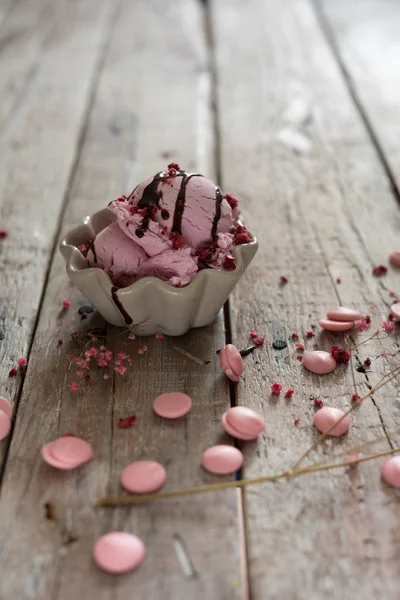 A scoop of homemade raspberry ice cream in a bowl and pink chocolate drops on old fashioned wooden table — Stock Photo, Image