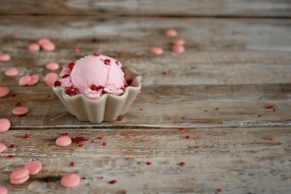 A scoop of homemade raspberry ice cream in a bowl and pink chocolate drops on vintage wooden background — Stock Photo, Image