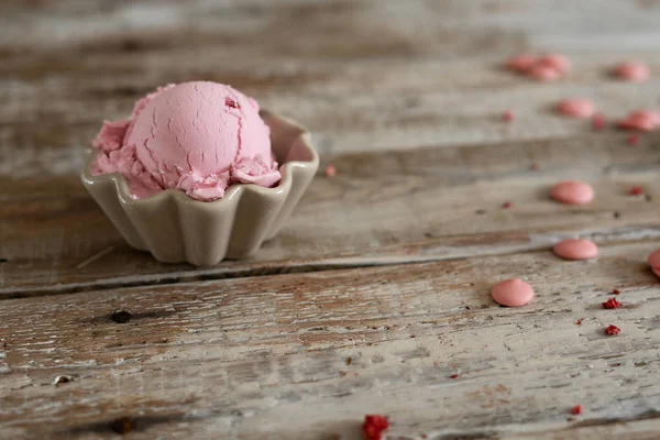 A scoop of homemade raspberry ice cream in a bowl and pink chocolate drops on old fashioned wooden table. Summer mood — Stock Photo, Image