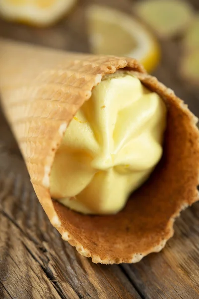 ginger lemon ice cream in a waffle cone with fresh lemons and ginger slices on a dark wooden background of boards