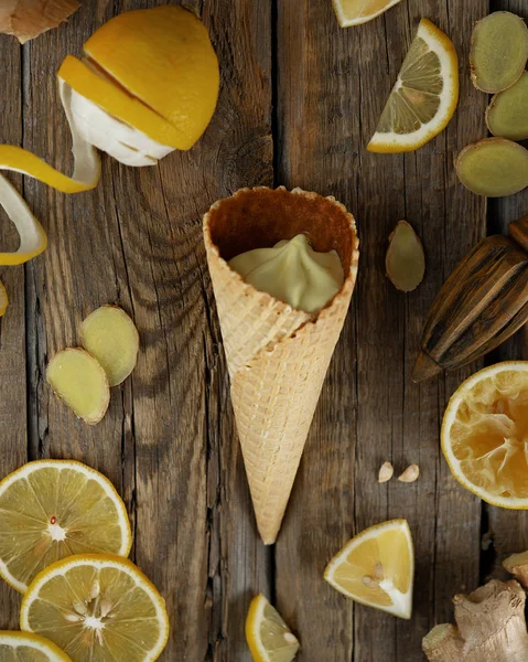 ginger lemon ice cream in a waffle cone with fresh lemons and ginger slices on a dark wooden background of boards. Closeup. Dark background, top view