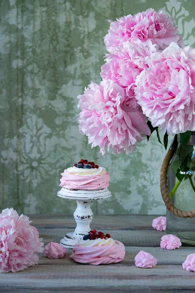 Pavlova cakes with cream and fresh summer berries. Close up of Pavlova dessert on vintage ceramic plate. peonies flowers. Food photography. Cook book or menu concept