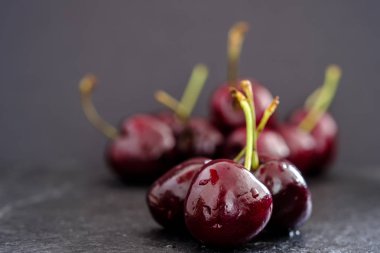 Üç sulu olgun koyu kırmızı kiraz yüzeyinde rustik kayrak ile odak grup siyah arka plan dışında