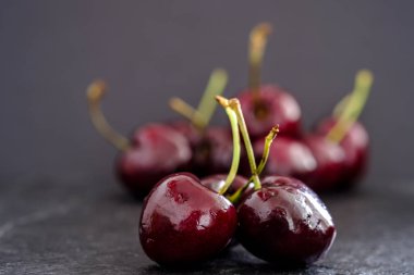 Üç sulu olgun koyu kırmızı kiraz yüzeyinde rustik kayrak ile odak grup siyah arka plan karşı dışında ön planda closeup