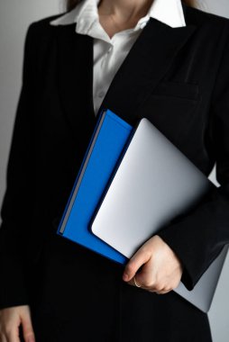 Resmi giyinmiş bir kadının elinde dizüstü bilgisayarla çekilmiş dikey fotoğrafı. Modern kariyer, liderlik ve teknoloji kavramı. 