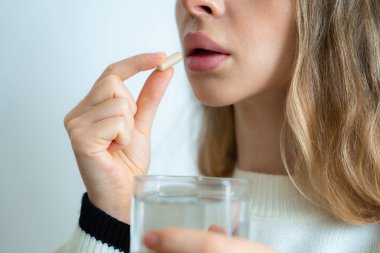 Ağzının yanında bir bardak suyla hap tutan bir kadın. Kişisel sağlık hizmetleri kavramı. 