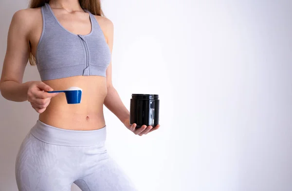 Gri spor kıyafetli bayan sporcu elinde bir kavanoz dolusu malzeme tutuyor. Protein, takviye ve fitness besin kavramı. 