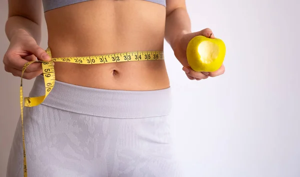 Kadın bir elmayı tutarken belini bantla ölçer. Beslenme ve zindelik dengesi, sağlıklı seçimler, diyet dostu yaşam tarzı. 