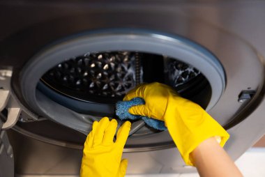  Yellow-gloved hand cleaning washing machine drum for maintenance and hygiene. 