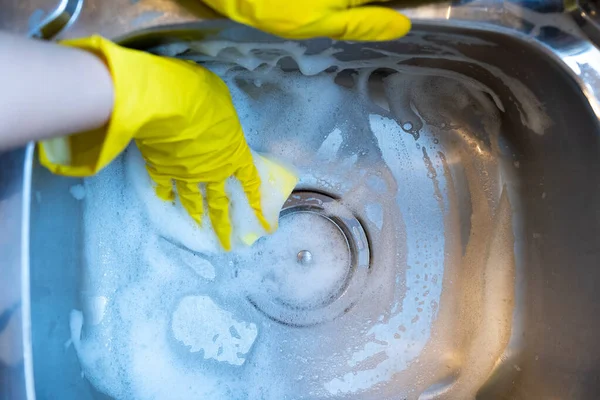 Person in gloves scrubbing stainless steel sink with detergent foam. 