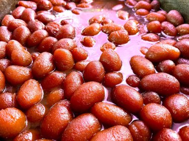 Yakın çekim, ışığın altında bile aromalı şuruba batırılmış birkaç gulab jamununu ortaya çıkarır; canlı renkler ve dokular yüksek çözünürlüklü fotoğraflarda yakalanır.