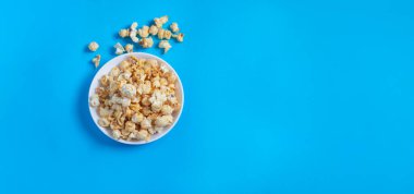 Beyaz yuvarlak seramik tabakta patlamış mısır, mavi, boş bir arka planda yan görüş. Yemek ve atıştırmalık kavramı,