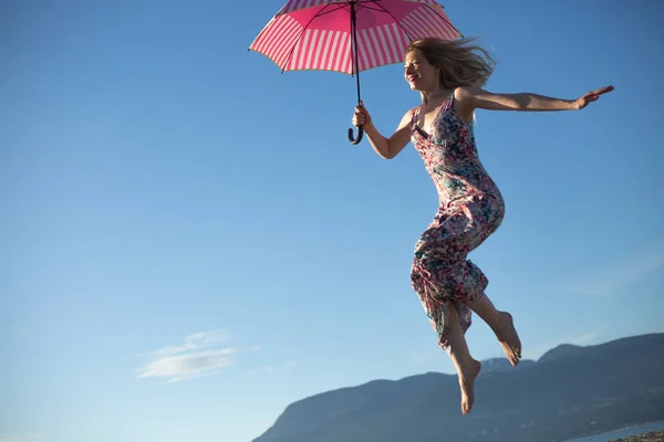 Young woman jumping holding pink umbrella — Stock Photo, Image