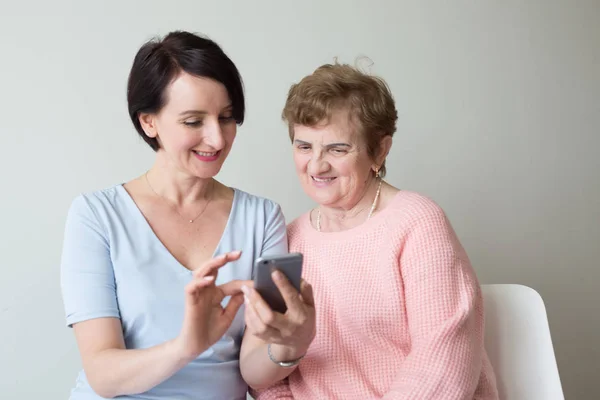 Ung kvinna hjälpa äldre kvinna med smartphone Royaltyfria Stockfoton