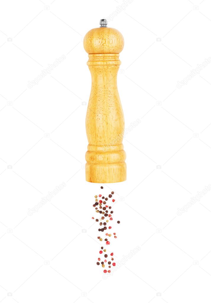 A mixture of peppers pouring from a wooden pepper shaker on a wh