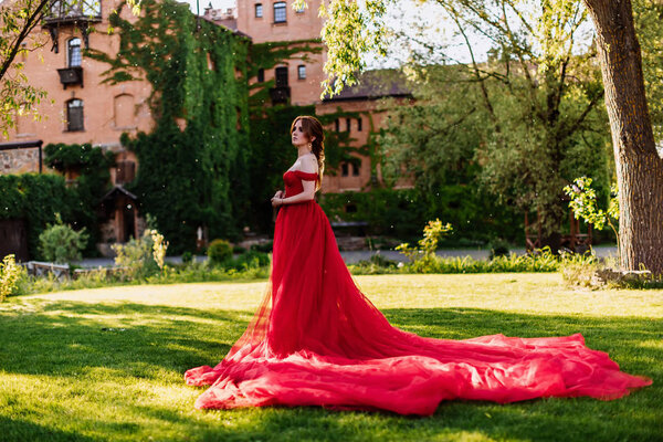 Рыжая женщина в красном платье возле замка
