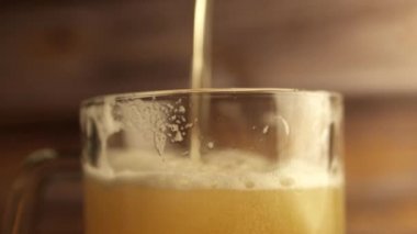 Yakın çekim bira bardağının içine dökülür, bir tutacağı, bir sürü köpük ve köpük bardaktan aşağı akar. Sıcak ahşap arkaplan