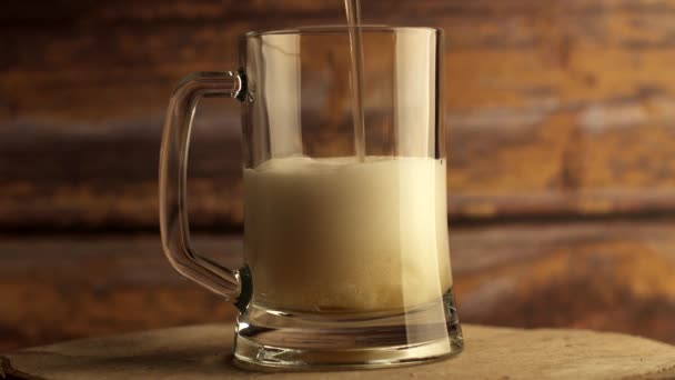 Beer is poured into a beer glass, a lot of bubbles and foam. Warm wooden background — Stock Video