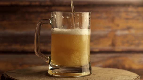 Μπύρα χύνεται σε ένα ποτήρι μπύρα με μια λαβή, πολλές φυσαλίδες και αφρό που ρέει κάτω από το ποτήρι. Ζεστό ξύλινο φόντο — Αρχείο Βίντεο