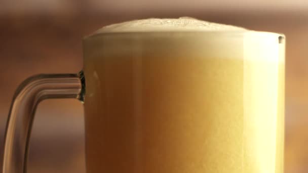 Primer plano de la cerveza se vierte en un vaso de cerveza con un mango, una gran cantidad de burbujas y espuma que fluye por el vaso. Fondo de madera caliente — Vídeos de Stock