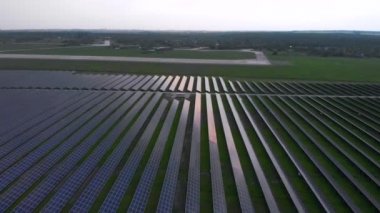 İnsansız hava aracı bulutlu bir yaz akşamında güneş panellerine doğru yavaş yavaş uçuyor. Güneş pili santralleri, yeşil çimenler. Görüntü 4k.