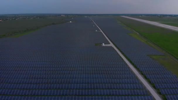 Blick aus der Luft in große Sonnenkollektoren auf einem Solarpark an bewölkten Sommerabenden. Solarzellenanlagen, grünes Gras. Videobeweis 4k. — Stockvideo