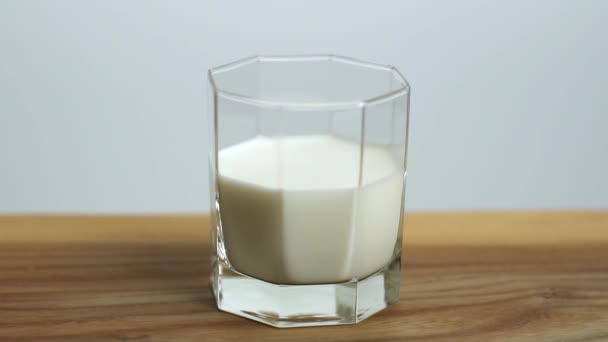 Φράουλα μούρο πέφτει σε ένα ποτήρι με γάλα σε αργή κίνηση. Πιτσιλιές γάλακτος σε ξύλινο τραπέζι. — Αρχείο Βίντεο