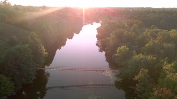 Zdjęcie lotnicze młodej sportowca jeździ rowerem po moście wiszącym nad rzeką o zachodzie słońca. Wesołych wakacji lub treningu w słoneczny letni dzień. Zdrowy styl życia rowerzystów — Wideo stockowe