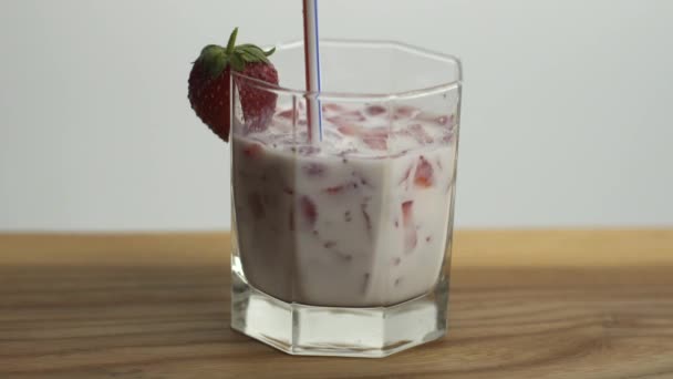 Quelqu'un boit du lait de fraise dans un verre avec tubule, préparant un cocktail de fruits dans la cuisine maison — Video