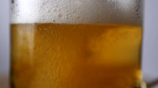 Крупный план светлого пива наливают в пивной стакан с ручкой, большим количеством пузырьков и пены — стоковое видео